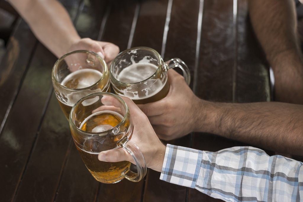 Três pessoas segurando copos de cerveja em comemoração