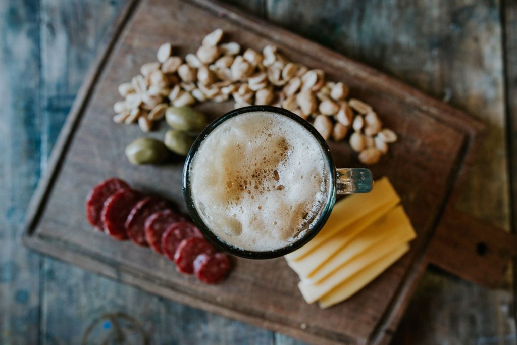 Queijo, amendoim e linguiça em uma tábua com um copo de cerveja