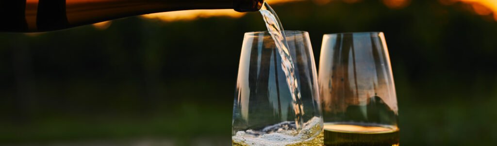 Taça com vinho branco envelhecido ao lado de garrafa de vinhos brancos antigos