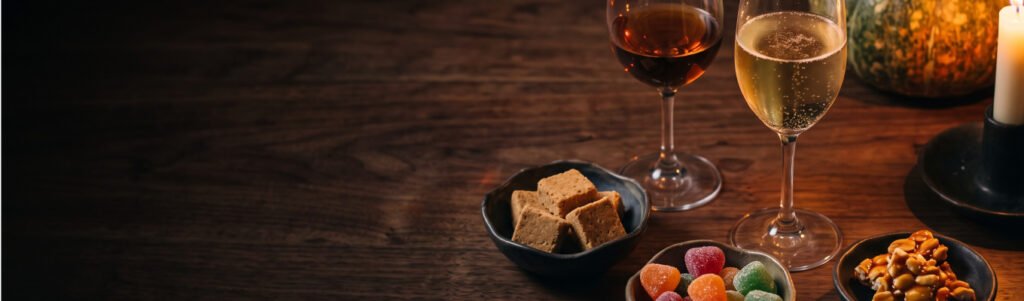 Taças de vinho do Porto e espumante ao lado de paçoca, jujubas e pé de moleque em mesa escura à luz de vela